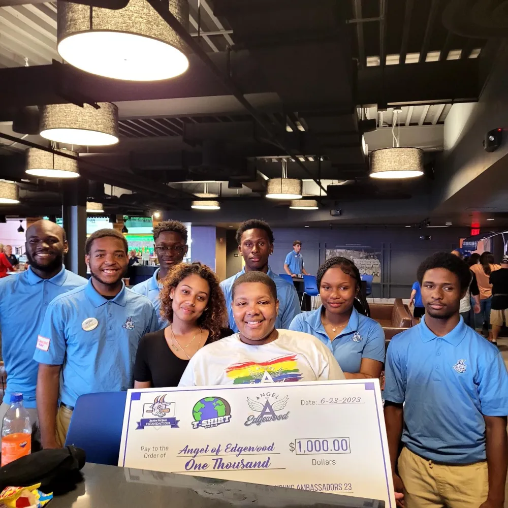 A group of individuals in blue shirts proudly holding a large check, smiling and celebrating their achievement together.