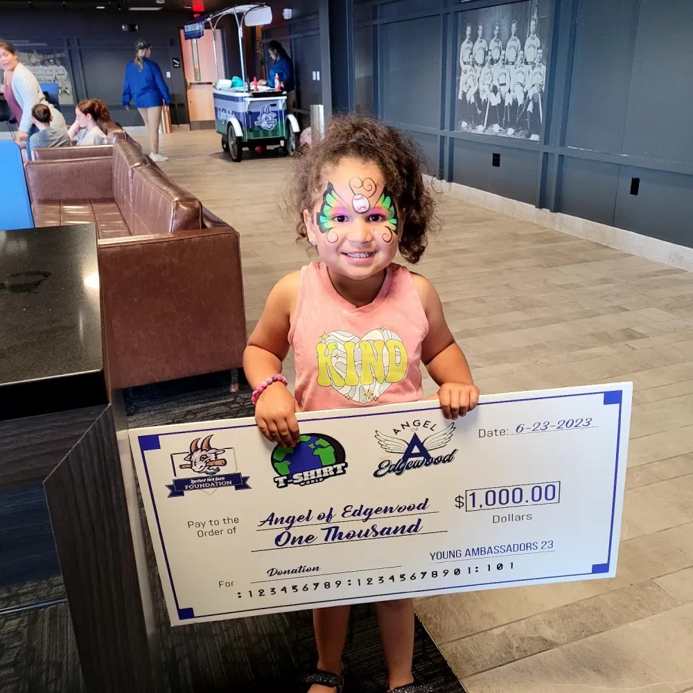 A young girl stands holding a check for $10,000, her face lit up with happiness.